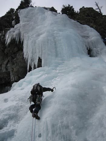 Alpiniste équipé de piolets et crampons, encordé avec un baudrier, escaladant activement une cascade de glace, avec son sac à dos Alpiniste équipé de piolets et crampons, encordé avec un baudrier, escaladant activement une cascade de glace, avec son sac à dos