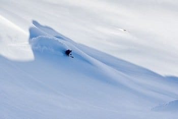 Skieur seul glissant au milieu de neige fraîche, sans rocher à l'horizon, sous l'ombre imposante de la montagne. Skieur seul glissant au milieu de neige fraîche, sans rocher à l'horizon, sous l'ombre imposante de la montagne.
