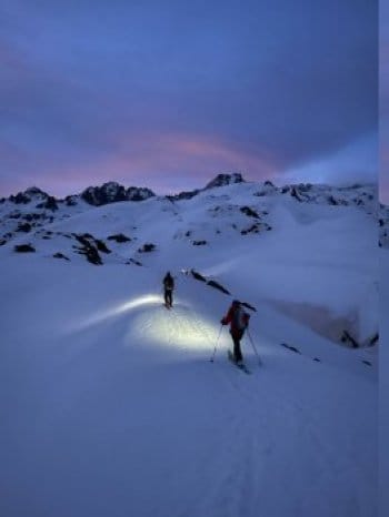 Deux skieurs en ski de randonnée rentrant au crépuscule, éclairés par des lampes frontales, sous un ciel aux teintes rosées et bleues sur les hauteur de Puyvalador. Deux skieurs en ski de randonnée rentrant au crépuscule, éclairés par des lampes frontales, sous un ciel aux teintes rosées et bleues sur les hauteur de Puyvalador.